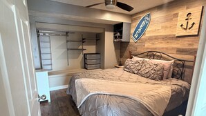 Quarto com cama, ventilador de teto, piso de madeira e uma parede com um aviso.
