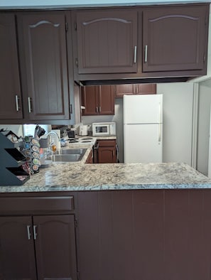 A kitchen with brown cabinets, a white refrigerator, a microwave, and a granite countertop. - The Cozy Retreat
Comfort, Fun & Convenience
(Windsor Heights)