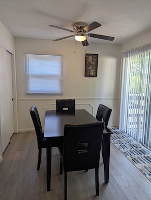 A dining area with a ceiling fan, a table with chairs, a window with blinds, and a door. - The Cozy Retreat
Comfort, Fun & Convenience
(Windsor Heights)