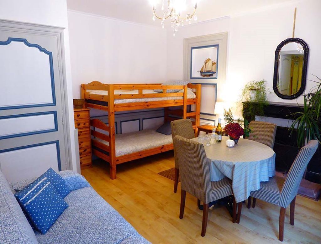 Une chambre avec un lit superposé, une table à manger avec des chaises, un canapé et un lustre.