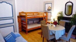 Una habitación con literas, una mesa de comedor con sillas, un sofá y una araña.