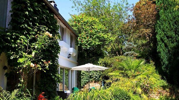 Una casa con jardín, un patio con mesa y sillas, y un paraguas grande.