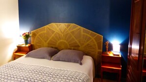Habitación de hotel con cama, mesita de noche con lámpara, puerta de madera y pared con diseño geométrico.
