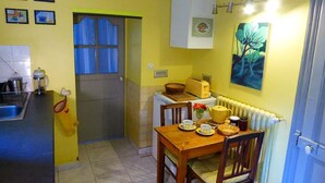 Cocina compacta con mesa, sillas, un radiador y una puerta con cortinas.