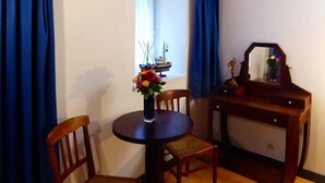 Un comedor con una mesa, sillas, un florero con flores, un escritorio de madera y una ventana con cortinas.