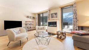 Ein modernes Wohnzimmer mit Flachbildfernseher, Kamin und großem Fenster mit Blick auf die Berge.