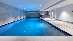 Ein modernes Hallenbad mit glasklarer, blauer Wasserfläche, umgeben von Wandflächen in neutralen Tönen und einem gefliesten Boden.