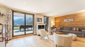 Ein geräumiges Wohnzimmer mit einem großen Schiebeglasfenster, das auf eine Terrasse führt, mit Kamin, einer Couch und einem Couchtisch.