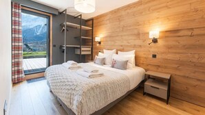 Ein Schlafzimmer mit Bett, Nachttischen, einer Holzwand und Bergblick durch eine Glastür.