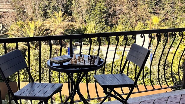 Un balcón con mesa y sillas, vista a árboles y cielo despejado.
