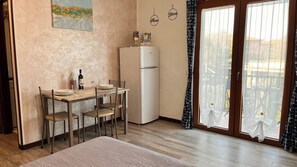 A kitchen with a dining table, chairs, a refrigerator, and a window with curtains. - Bright studio apartment with balcony, ideal for moments of pure relaxation. (Peschiera del Garda)
