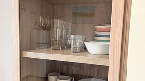 Un mueble de madera con puertas de cristal que contiene platos apilados, boles y vasos transparentes.