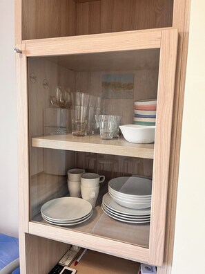 A wooden cabinet with glass doors containing stacked plates, bowls, and clear drinking glasses. - Bright studio apartment with balcony, ideal for moments of pure relaxation. (Peschiera del Garda)