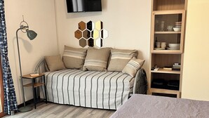Un dormitorio con cama, televisor, estantería y lámpara de pie.
