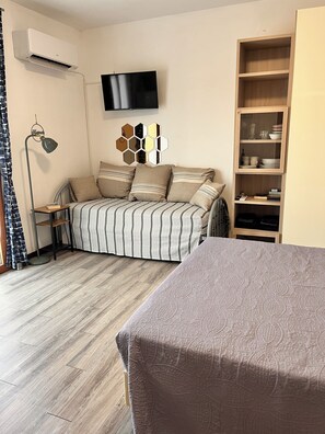 A bedroom with a bed, a TV, a bookshelf, and a floor lamp. - Bright studio apartment with balcony, ideal for moments of pure relaxation. (Peschiera del Garda)