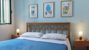 Ein ordentlich bezogenes Bett mit blauer Bettdecke, zwei Nachttischlampen und drei gerahmte Kunstwerke an der Wand.