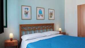 Ein Schlafzimmer mit einem Holz-Kopfteil, einem Bett mit weißer und blauer Bettwäsche, zwei Nachttischlampen und drei gerahmten Kunstwerken an der Wand.