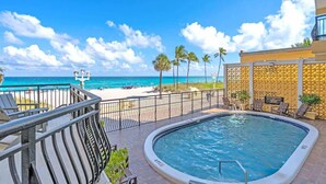 A pool area with a view of the beach and ocean, a fenced deck, and lounge chairs. - Oceanfront 2BR/2BA · Pool, Free Parking + Views (Hollywood)