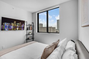Une chambre moderne avec un grand lit, une vue sur la ville, une bibliothèque et une fenêtre.