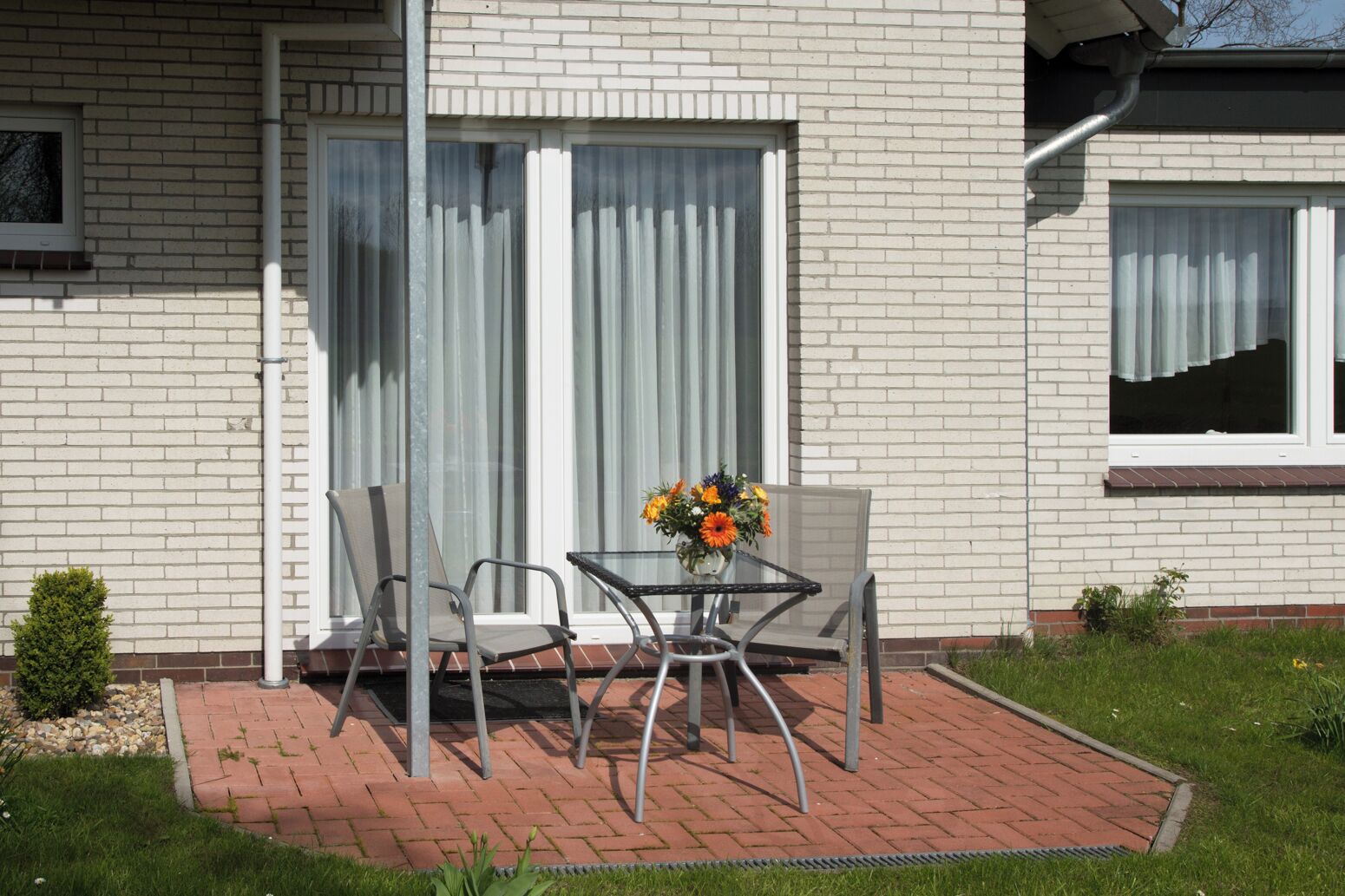 Une maison avec un patio, une table et des chaises, et un vase à fleurs.
