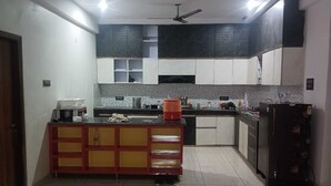 A kitchen with a central island, cabinets, a refrigerator, and a ceiling fan. - Hotel Vivara (Lucknow)