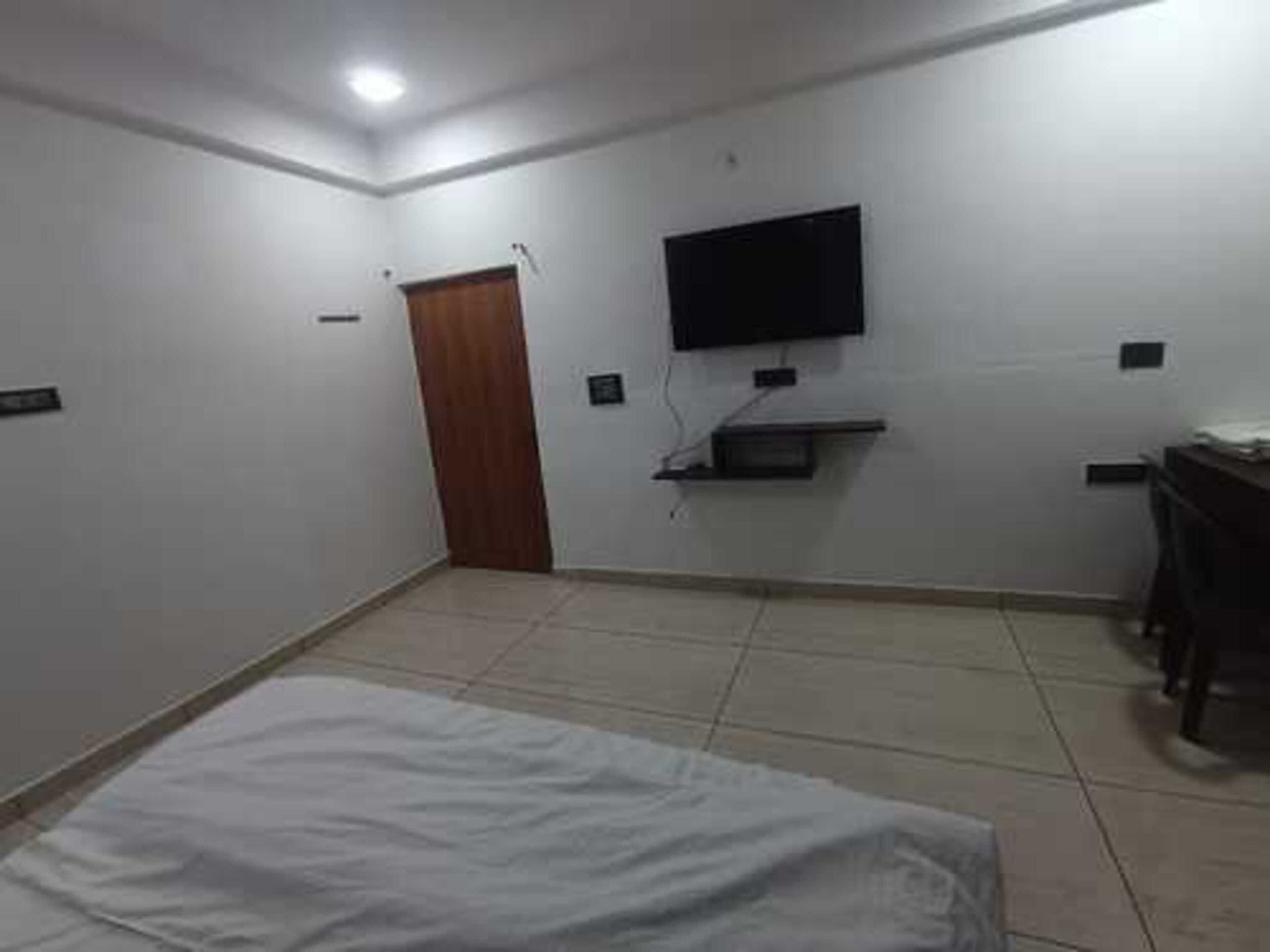 A room with a bed, a television mounted on the wall, a small shelf, and a door.