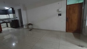 A spacious room with a tiled floor, a wooden door, and a small table with a chair. - Hotel Vivara (Lucknow)