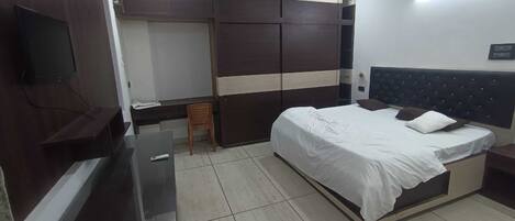 A bedroom with a bed, a TV, a desk, and a wardrobe.