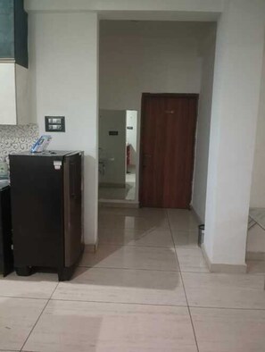 A hallway with a refrigerator, a door, and a tiled floor. - Hotel Vivara (Lucknow)