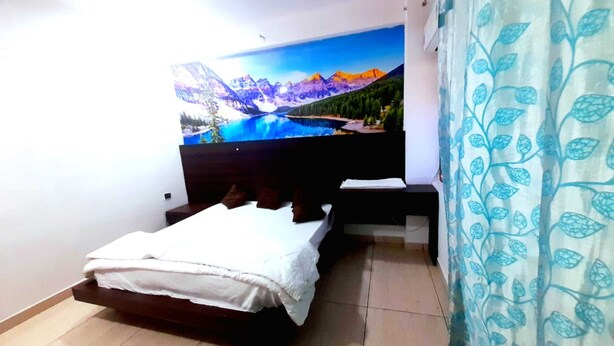A bedroom with a bed, a nightstand, a TV mounted on the wall, and a curtain with a leaf pattern. - Hotel Vivara (Lucknow)