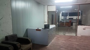 A reception area with a reception desk, a seating area with chairs, and a view into a kitchen area. - Hotel Vivara (Lucknow)