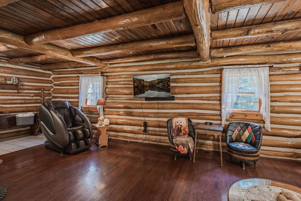 Interior de cabana de tronco com uma cadeira de massagem, uma mesinha e uma poltrona com almofada colorida.