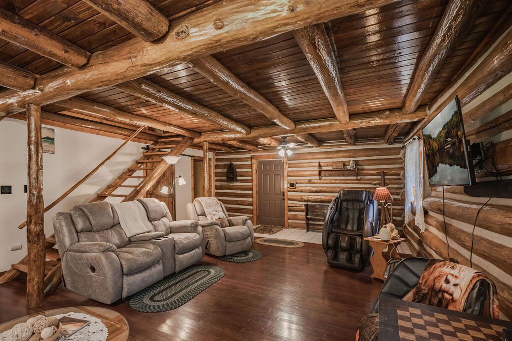 A log cabin interior with a wooden ceiling, a reclining sofa, a leather armchair, a television, and a fireplace.