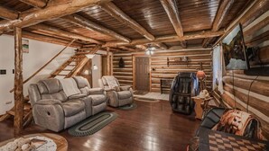 A log cabin interior with a wooden ceiling, a reclining sofa, a leather armchair, a television, and a fireplace. - Stepping Back in Time Getaway: Hot Tub + Wifi (South Bloomingville)