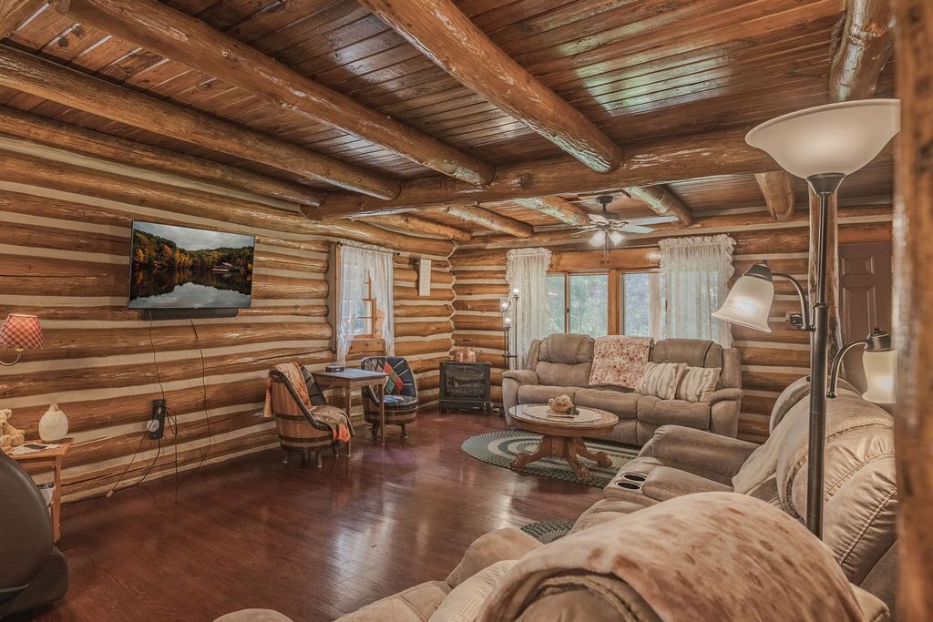 Ein Blockhaus-Interieur mit Holzbalkendecke, einem montierten Fernseher, einem Kamin und einer gemütlichen Sitzecke.