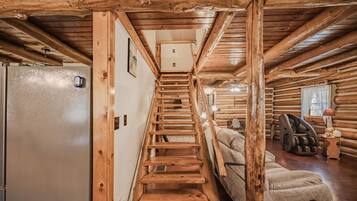 A log cabin interior with a wooden staircase leading to a loft bedroom, a sofa, and a massage chair.