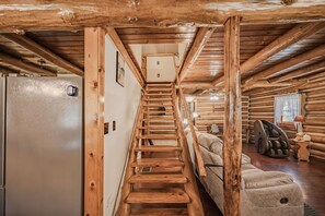 L’intérieur d’une cabane en rondins, avec un escalier en bois menant à une chambre à l’étage, un canapé et un fauteuil de massage.