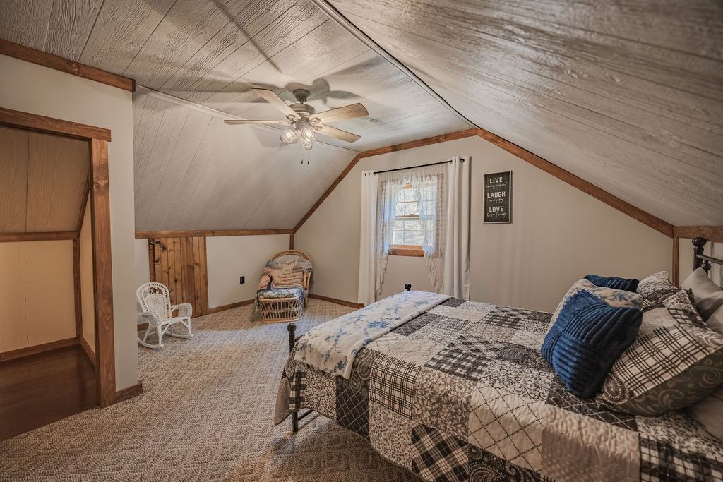 A bedroom with a sloped ceiling, a bed with patterned bedding, a chair, and a ceiling fan.
