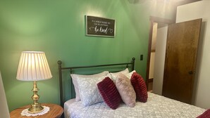 A bedroom with a green wall, a bed with patterned bedding, a bedside table with a lamp, and a motivational quote sign. - Stepping Back in Time Getaway: Hot Tub + Wifi (South Bloomingville)