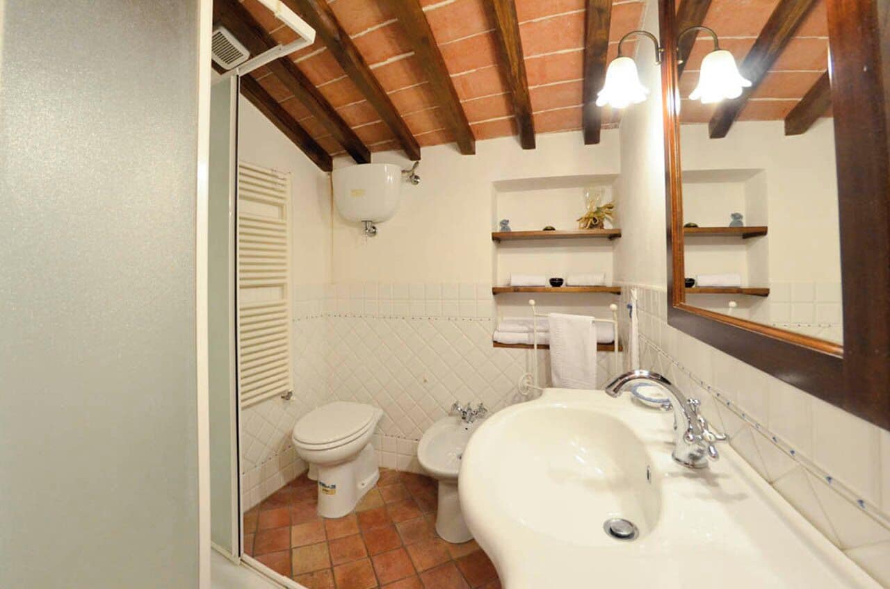 A bathroom with a toilet, bidet, and sink, wooden beams on the ceiling, and a mirror above the sink.