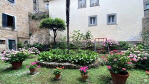 A courtyard with potted plants, a swing set, and stone buildings. - CASA AMBRA (Cortona)