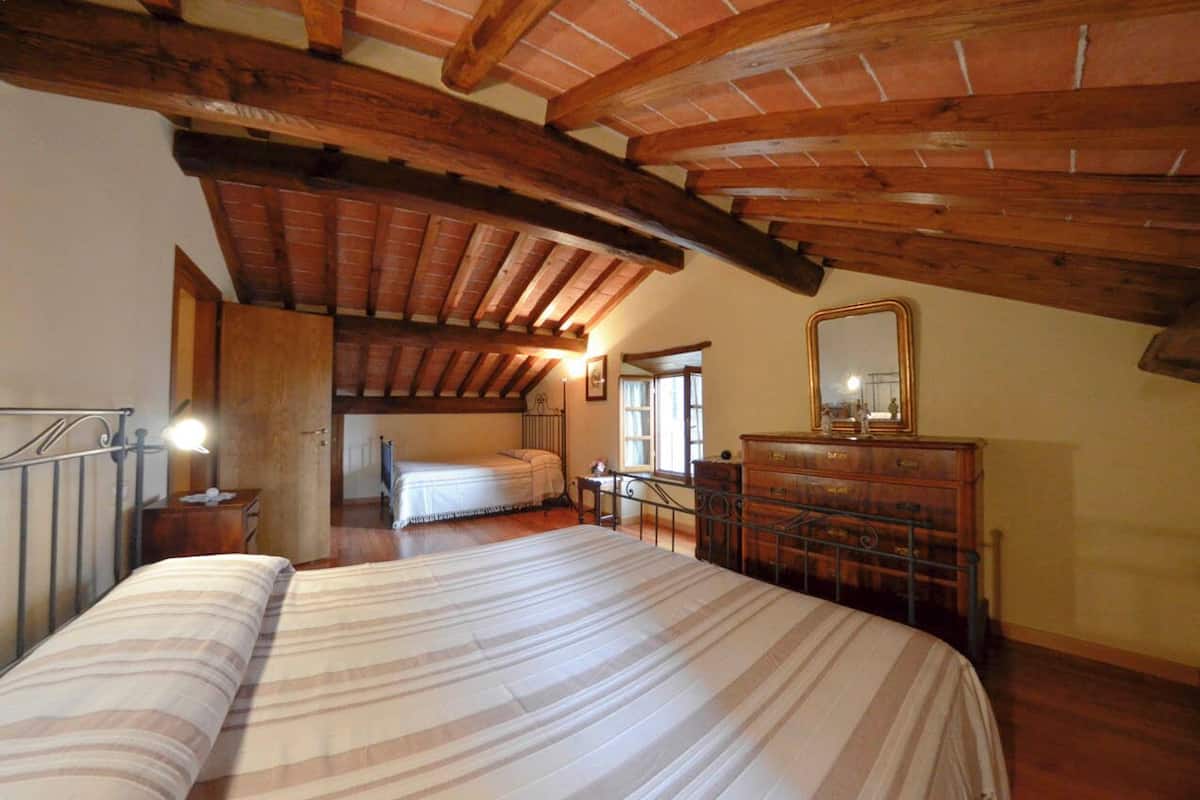 A bedroom with a large bed, wooden beams, a dresser, and a mirror.