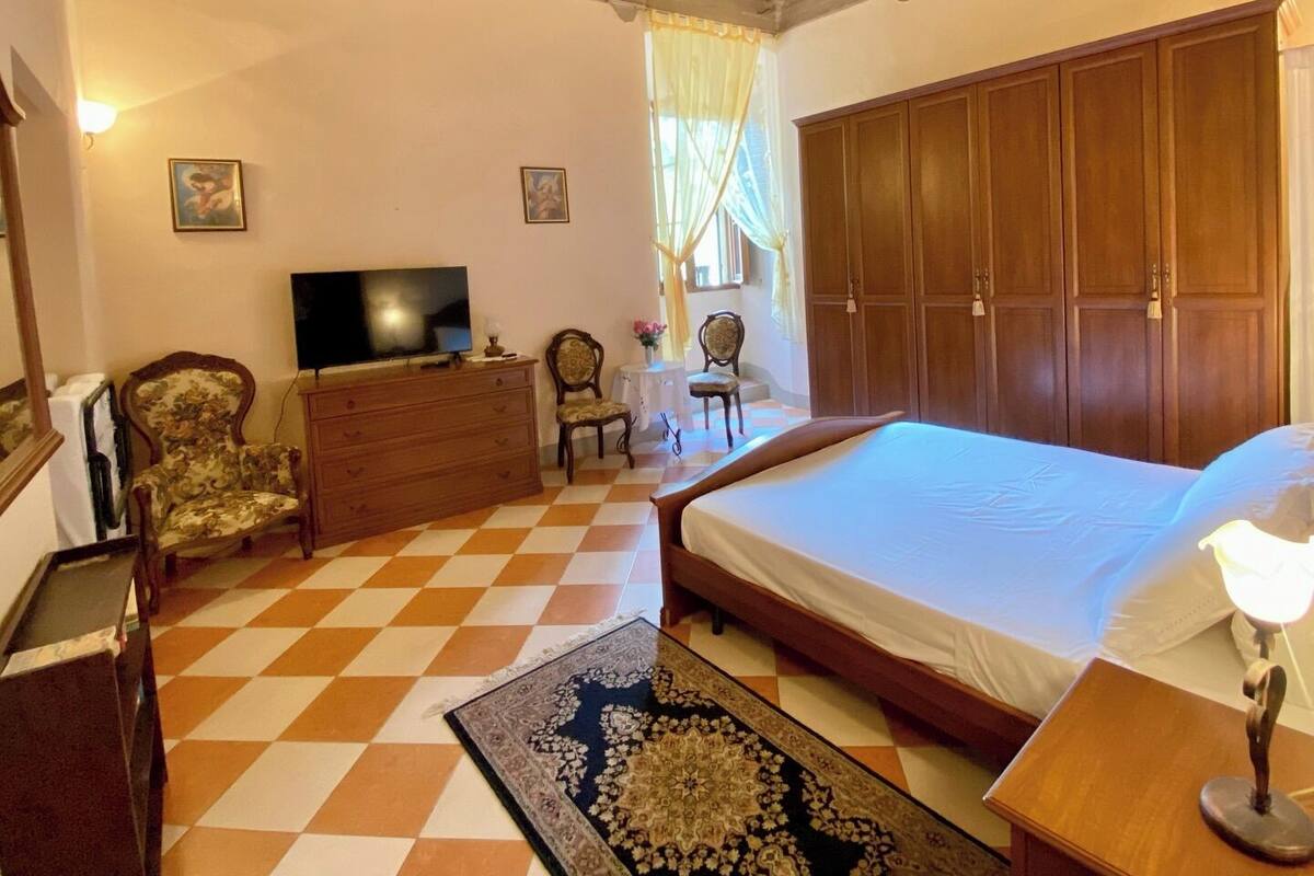 A bedroom with a checkered floor, a bed, a television, a dresser, and a wardrobe.