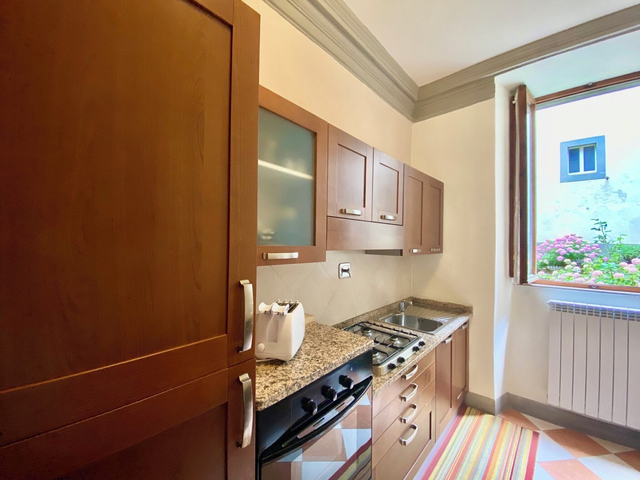 Una cocina compacta con armarios de madera, estufa y ventana con vistas a un jardín.