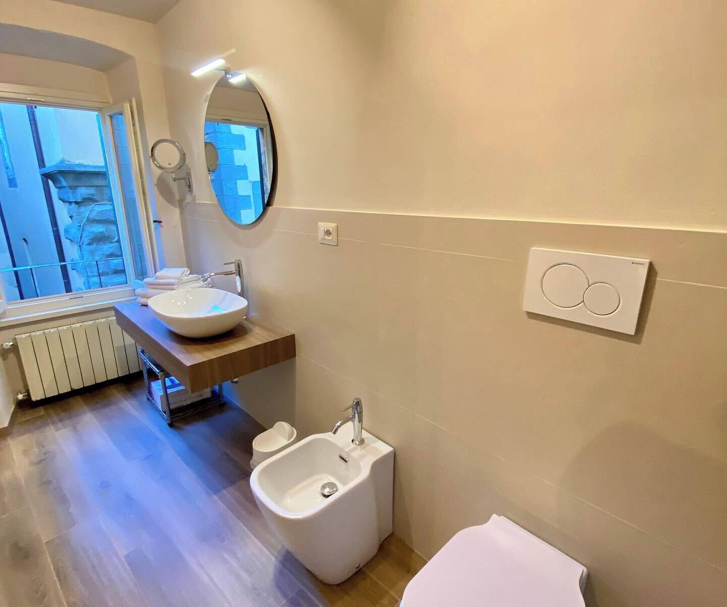 A bathroom with a round mirror, a sink, a bidet, and a towel rack.