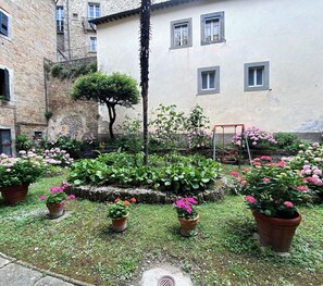 A courtyard with potted plants, a swing, and a stone building with windows.