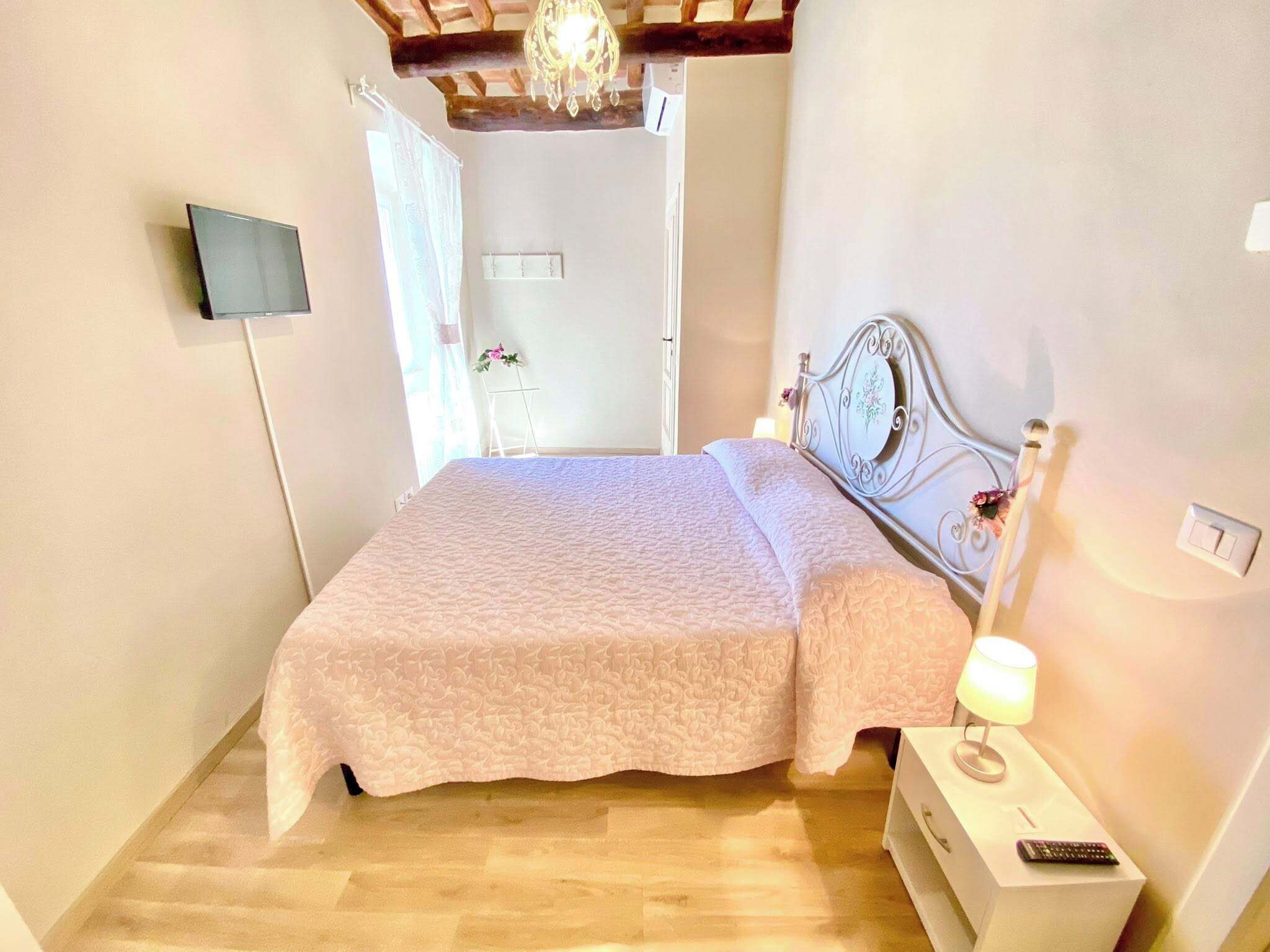 A bedroom with a bed, a nightstand, a lamp, a TV, and a chandelier.