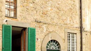A stone building with a green door, a window with shutters, and a small window with bars. - CASA AMBRA (Cortona)