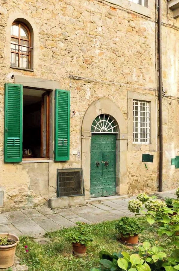 A stone building with a green door, a window with shutters, and a small window with bars.