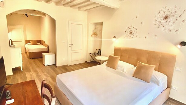 A hotel room with a large bed, a desk, a chair, a small table, and a door leading to another room. - CASA AMBRA (Cortona)